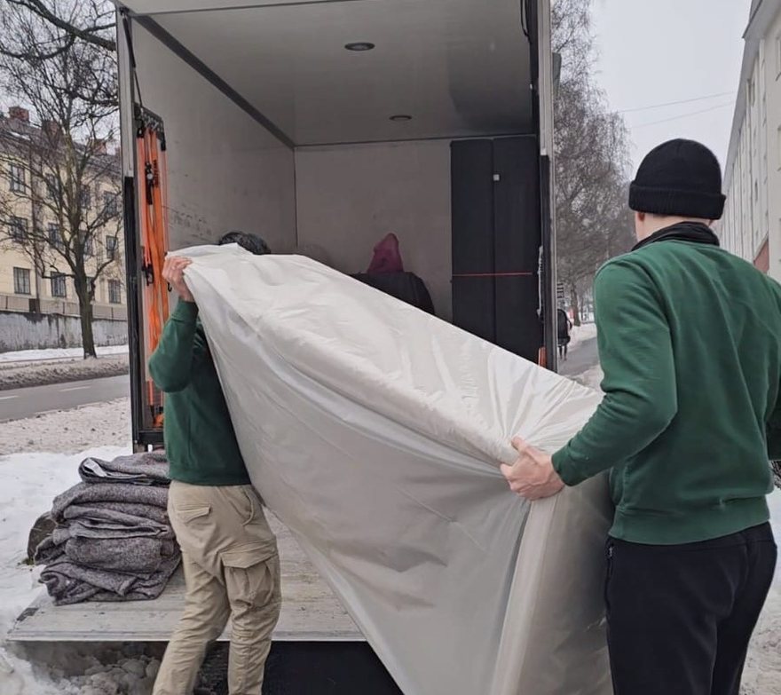 En madrass pakket i plast bæres inn i flyttebilen