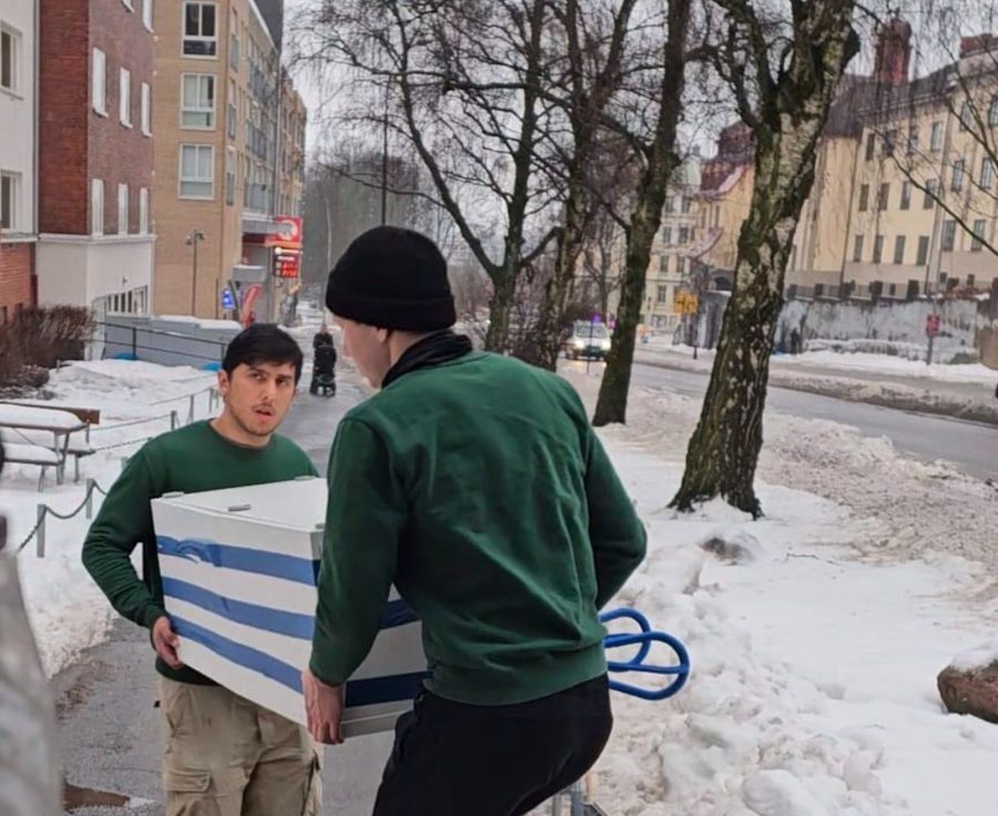 To fra mannskapet bærer et hvitevare ut til bilen i en gate i Oslo
